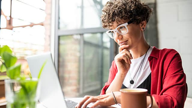 Busy young elegant woman in eyeglasses looking at laptop display