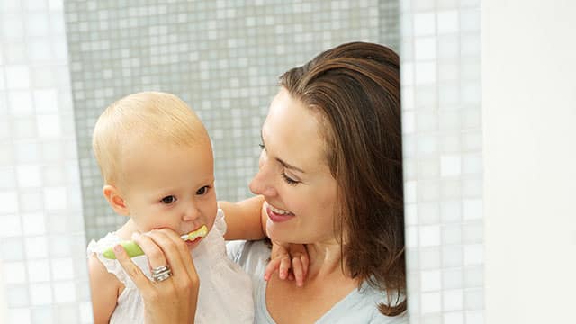 A mother is carrying their baby and brushing their teeth