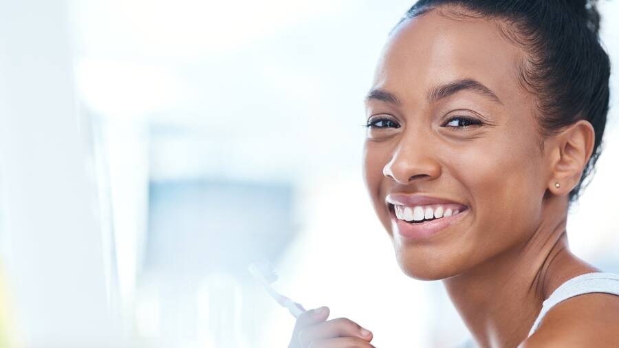 woman smiling while brushing her teeth