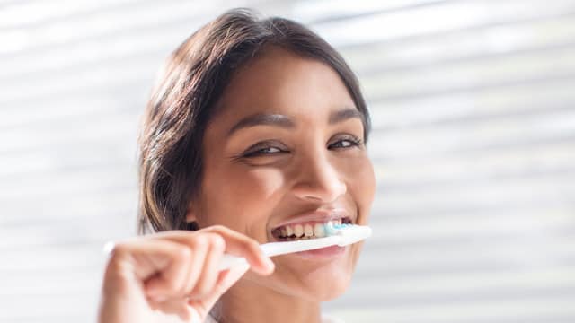 woman smiling while brushing her teeth