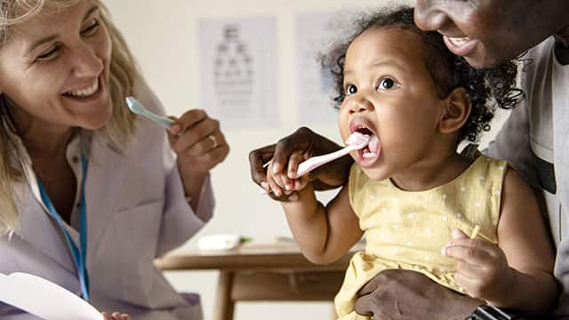 Dentist teaching a little girl how to brush her teeth