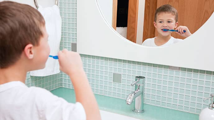 a boy looking at the mirror while brushing his teeth with Colgate toothpaste