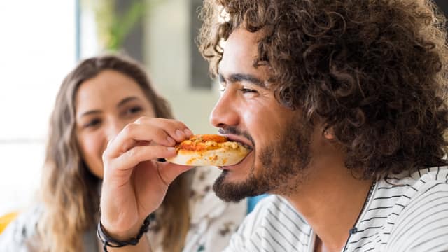 A man eating a pizza bagel A man with long curly hair and a beard eating a pizza bagel