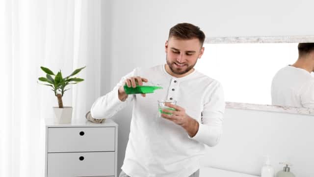 Young man pouring with mouthwash into small cup while standing in bathroom