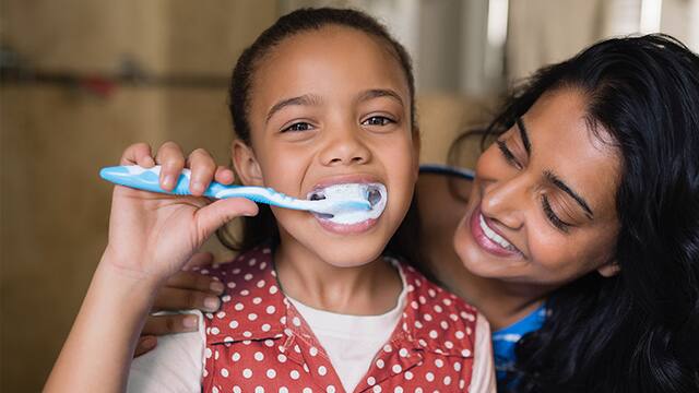Mujer sonriendo mientras su hija se cepilla los dientes