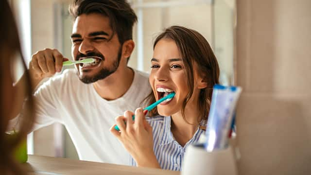 couple brushing teeth in bathroom mirror