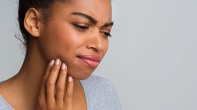 woman frowning holding her right jaw