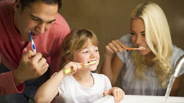 Young girl brushing her teeth with her parents