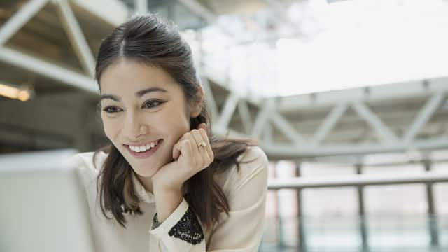a woman smiling while looking at the tablet with her hand on her chin