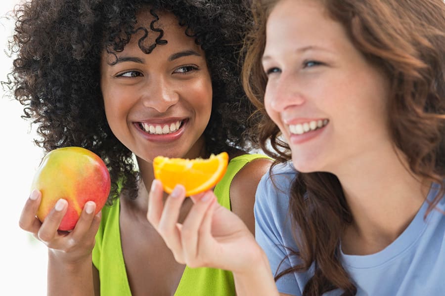 Close-up of two smiling female friends eating acidic fruits