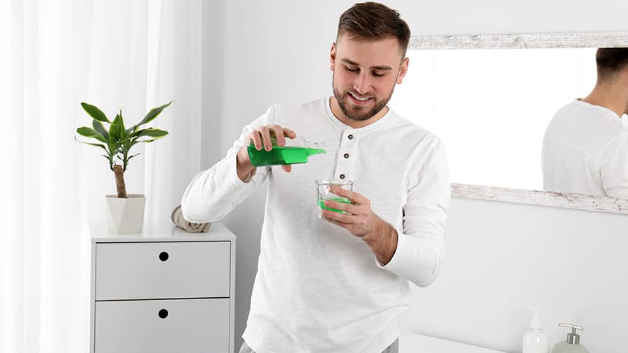  a young man is useing chlorhexidine gluconate mouthwash in the bathroom
