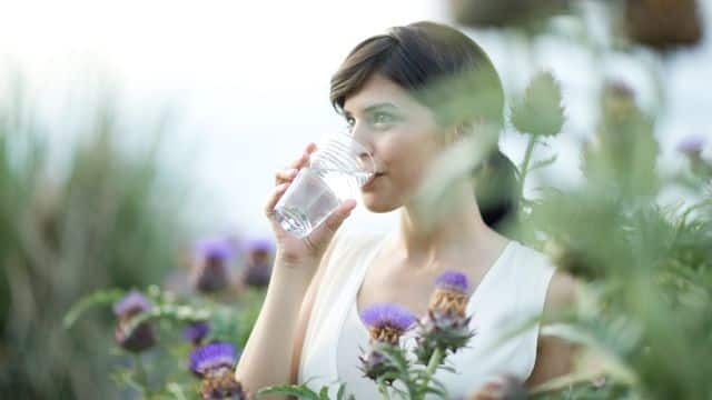 a woman drinking a glass of water out door in the garden