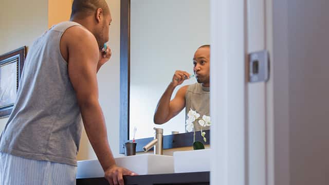 man brushing his teeth with Colgate toothbrush in front of mirror