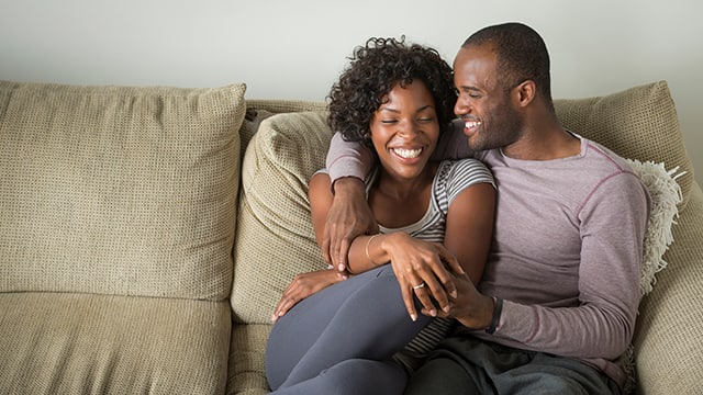 Couple smiling and in an intimate cuddle on a couch