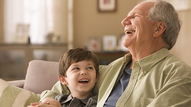 a grandfather and a grandson sitting next to each other while laughing