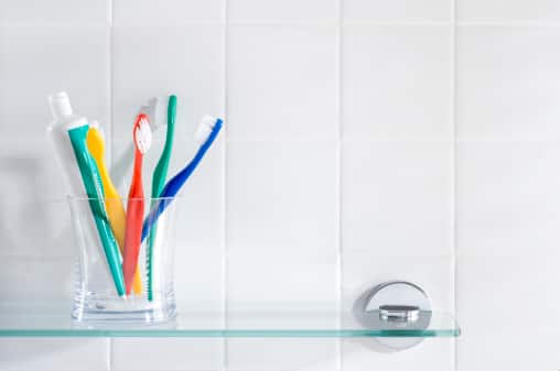 Toothbrushes and a tube of toothpaste in a glass cup on top of the bathroom shelf