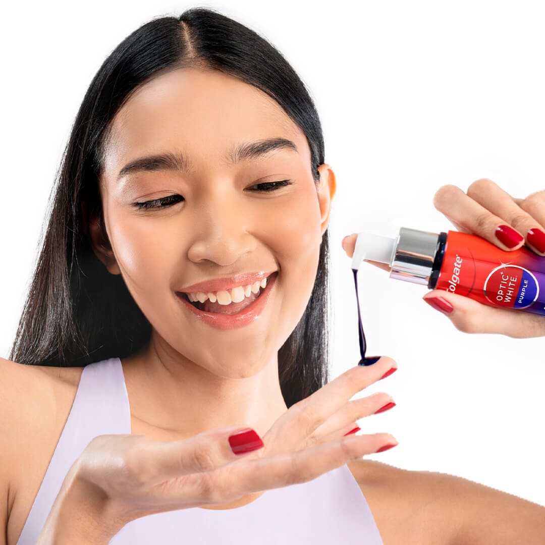 A smiling young girl pumping Purple Serum onto her finger with the Optic White Purple Serum bottle