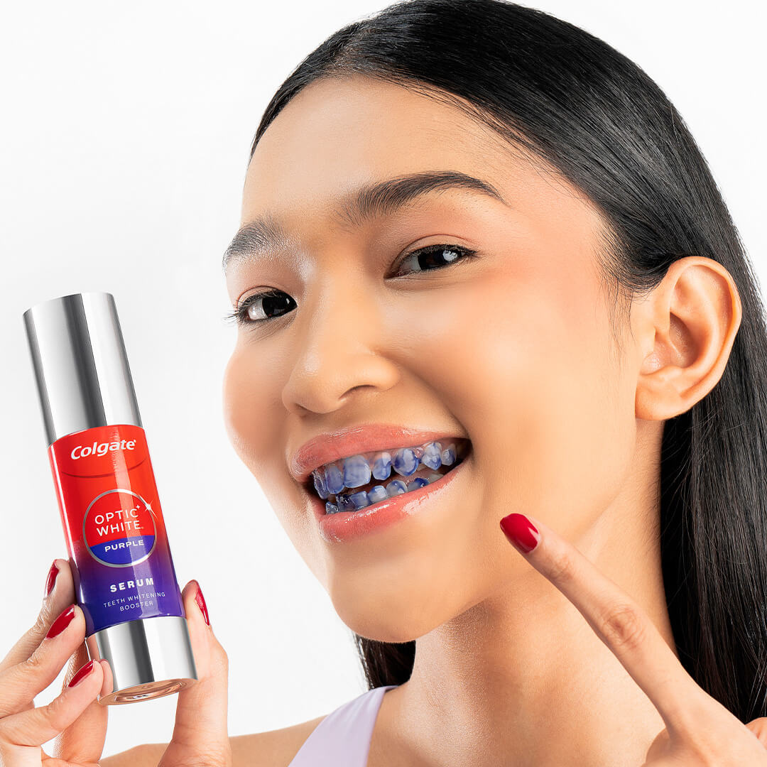 A young girl showing off the Optic White Purple Serum bottle and her teeth, which has been applied with the purple serum