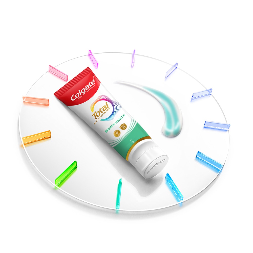 A Colgate Total toothpaste tube lying on a clock with a smatter of paste next to it