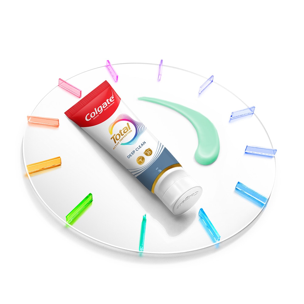 A Colgate Total toothpaste tube lying on a clock with a smatter of paste next to it