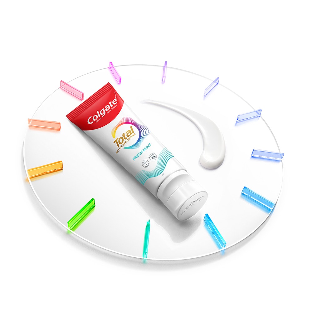 A Colgate Total toothpaste tube lying on a clock with a smatter of paste next to it