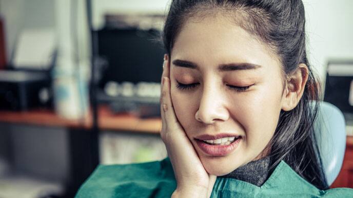 ผู้หญิงที่กำลังจับแก้มด้านขวาเพื่อเช็คอาการของฟันหลังจากผ่าฟันคุด