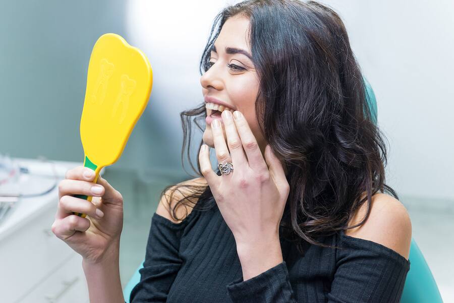 Young woman looking at her teeth using a hand-held mirror Young woman looking at her teeth using a hand-held mirror
