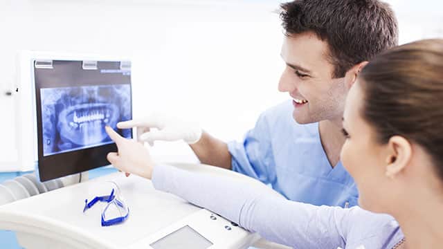 A male dentist is showing whole mouth x-rays to the female patient